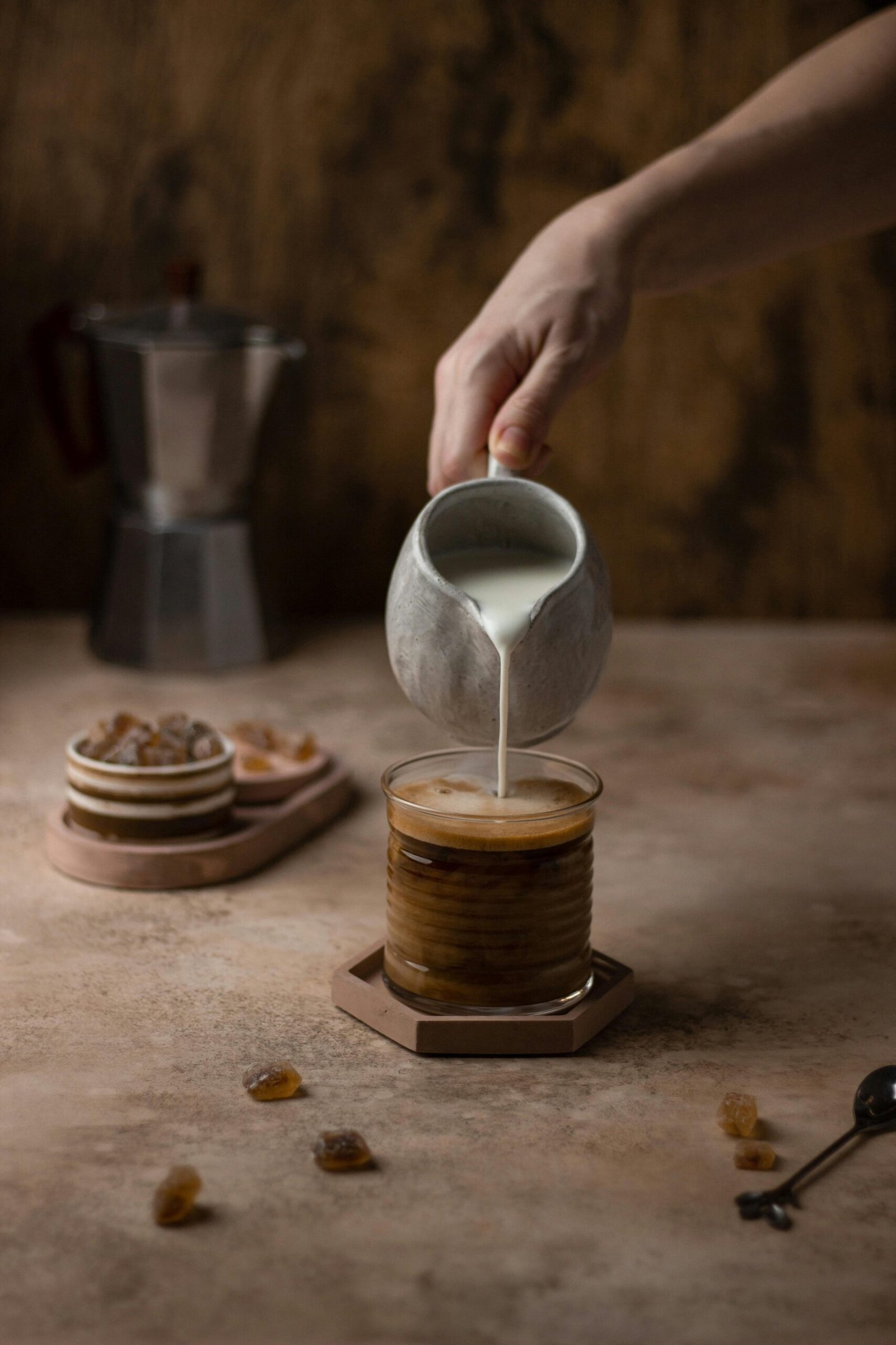 A close-up of milk being poured into coffee, captured in a rustic kitchen setting.